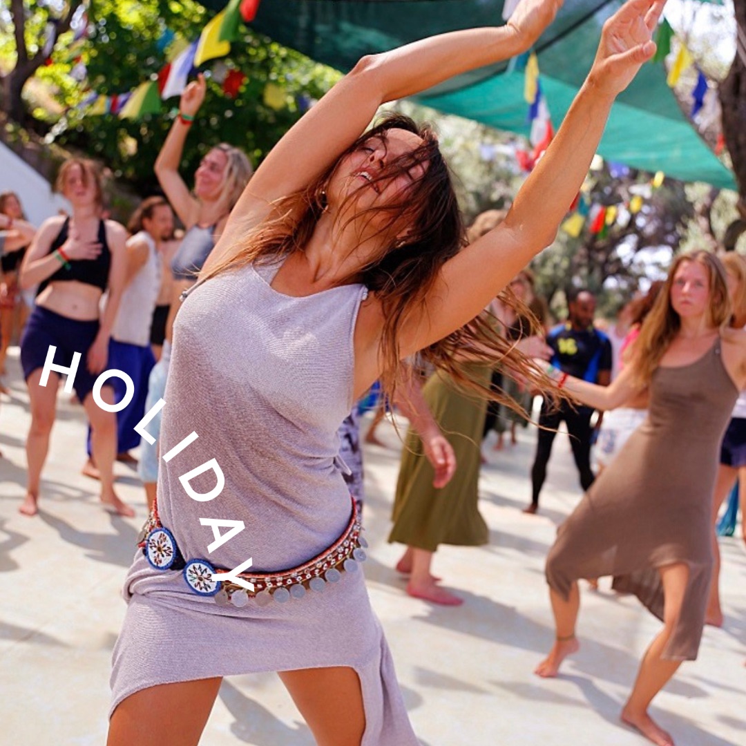 A dancer raises her arms among people dancing outdoors beneath colourful flags